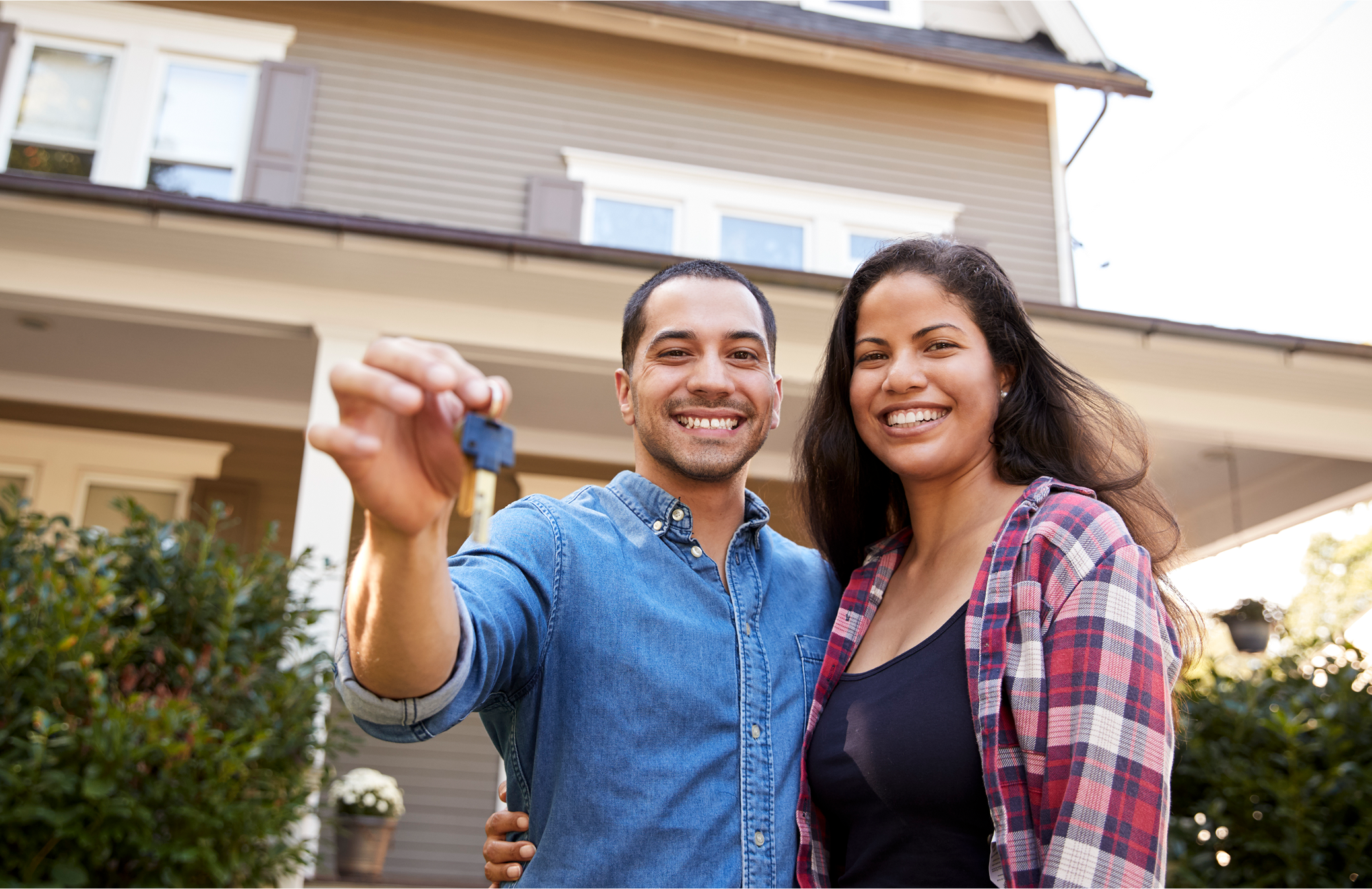 Smiling couple holding a key in front of their new home